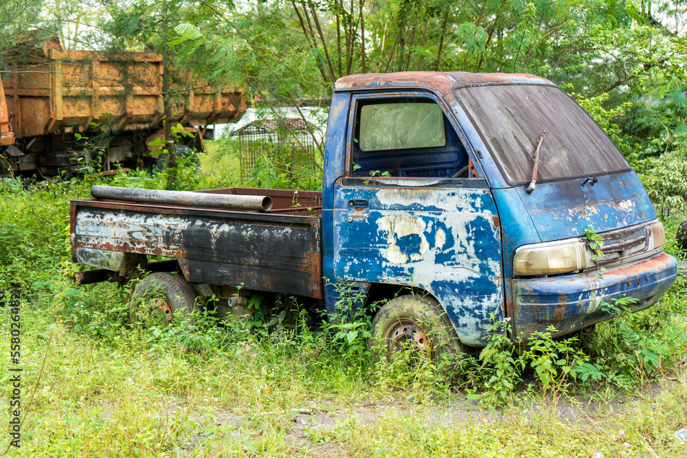 Side view of an abandoned blue pick up vehicle stay strong with a truck in the background Side view of an abandoned blue pick up vehicle stay strong with a truck in the background