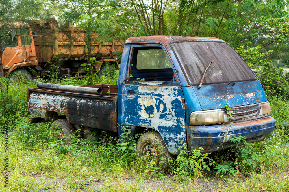 Side view of an abandoned blue pick up vehicle stay strong with a truck in the background