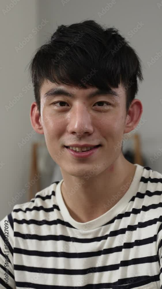 Vertical Screen: shoulder shot portrait of an asian handsome young man turning to smile at the camera while learning from home on the computer in the bedroom. Vertical Screen: shoulder shot portrait of an asian handsome young man turning to smile at the camera while learning from home on the computer in the bedroom.