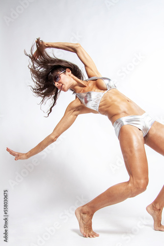 Latin woman with tanned skin and impressive muscular body moving hair while posing with sunglasses on a white background in bikini. Fitness, bodybuilding, aerobics, concept. Copy space, vertical.