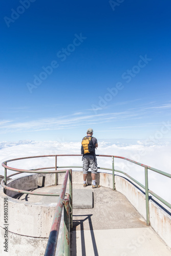 tourist with yellow backpack at a viewpoint with a view of a volcano crater in Irazu Volcano National Park in Costa Rica on a sunny day