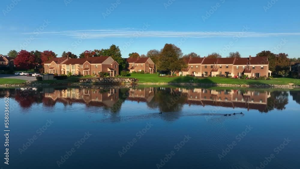 American city suburb with peaceful lake view. Autumn fall foliage and leaves on trees. Calm water reflects apartment unit building housing. American city suburb with peaceful lake view. Autumn fall foliage and leaves on trees. Calm water reflects apartment unit building housing.