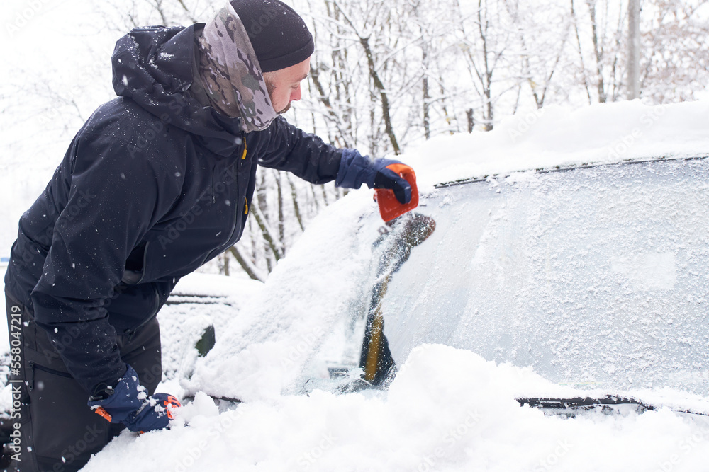   Man cleans his car after a snowfall. Cleaning snow from windshield, Scraping ice, Winter car window cleaning