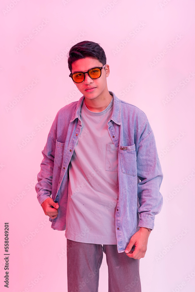 A cool asian guy wearing shades and in a gray T-shirt and blue denim jacket. Posing behind a plain background with hot pink neon effect. A cool asian guy wearing shades and in a gray T-shirt and blue denim jacket. Posing behind a plain background with hot pink neon effect.