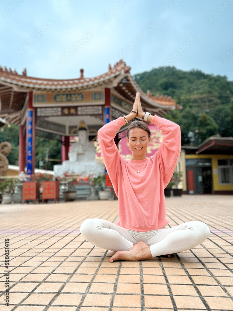 Fototapeta premium Young beautiful meditating woman in buddhist temple in lotus pose with hands in Namaste position