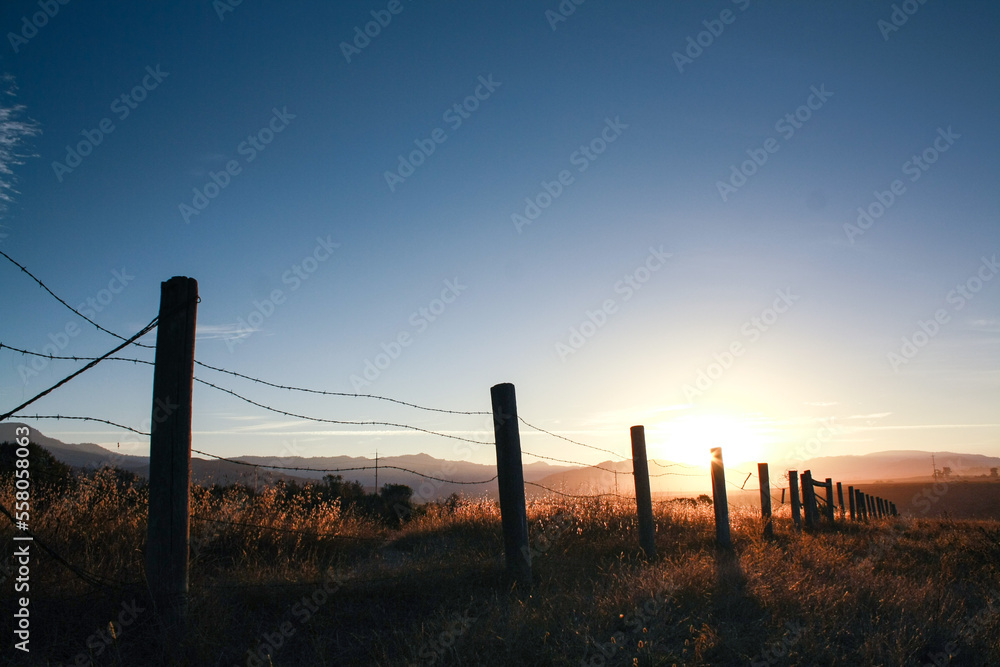 Barbed wire fence with wooden post at sunset