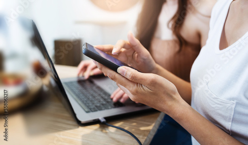 Two of young asian woman working on laptop and using mobile phone to searching data for her new business from internet