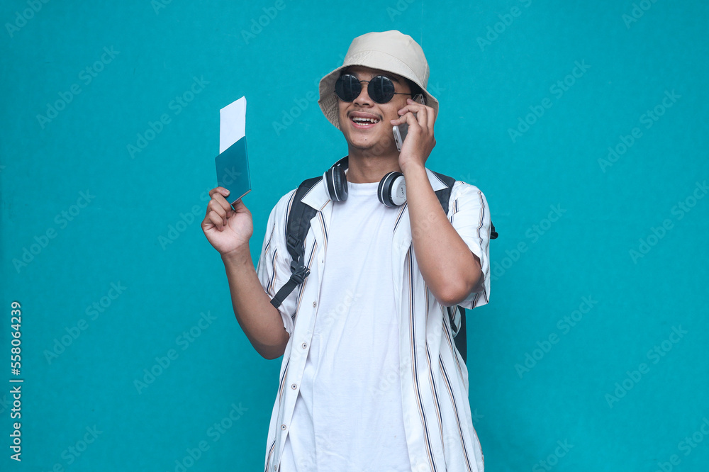 Happy young tourist holding passport and boarding tickets while having a phone call