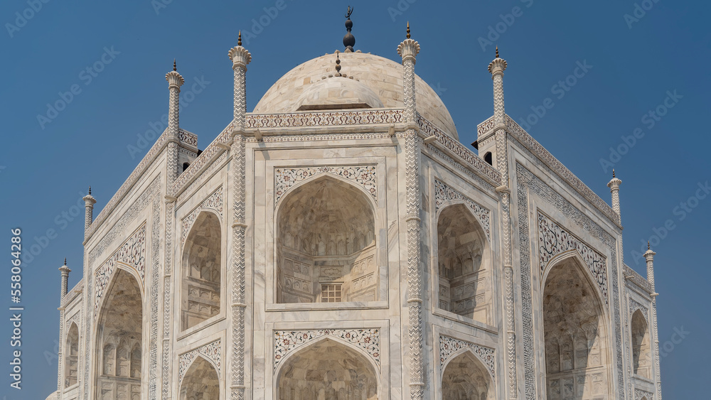 A beautiful old mausoleum of the Taj Mahal against the blue sky. The white marble building with arches, balconies, domes and spires is decorated with carvings, inlays of precious stones. India. Agra
