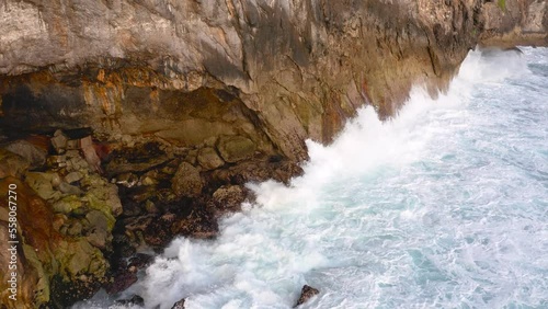 Areal shot of angry white waves crashing into the beautiful rocky cliffside of Nusa Penida Guyangan Falls photo