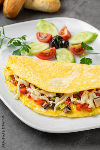 Omelet with cheese, mushrooms and vegetables on a white porcelain plate