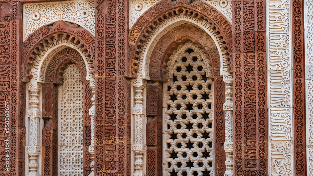The ancient temple complex of Qutub Minar. Details. The facade is made of red sandstone and white marble decorated with carved ornaments. The arched windows have decorative stone grilles. India. Delhi