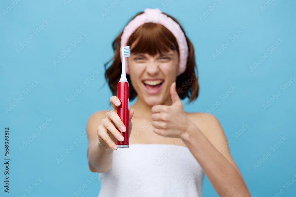 a young woman is standing in a white towel facing the camera, holding a red toothbrush in her hand and holding it out to the viewer, smiling broadly and showing a thumbs up. a young woman is standing in a white towel facing the camera, holding a red toothbrush in her hand and holding it out to the viewer, smiling broadly and showing a thumbs up.