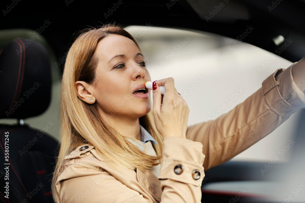 A stylish woman is putting lip balm while sitting in her car and looking at rear view mirror. A stylish woman is putting lip balm while sitting in her car and looking at rear view mirror.