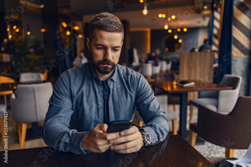 A young man is sitting in coffee shop and ordering drinks on mobile app.