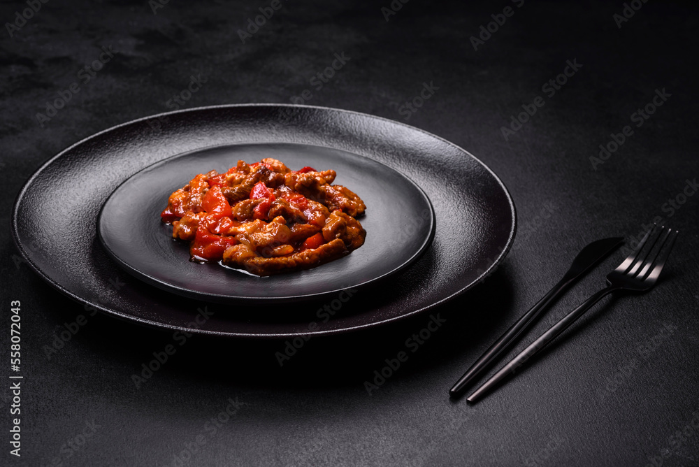 .Delicious juicy meat with hot peppers and sauce on a black ceramic plate .Delicious juicy meat with hot peppers and sauce on a black ceramic plate