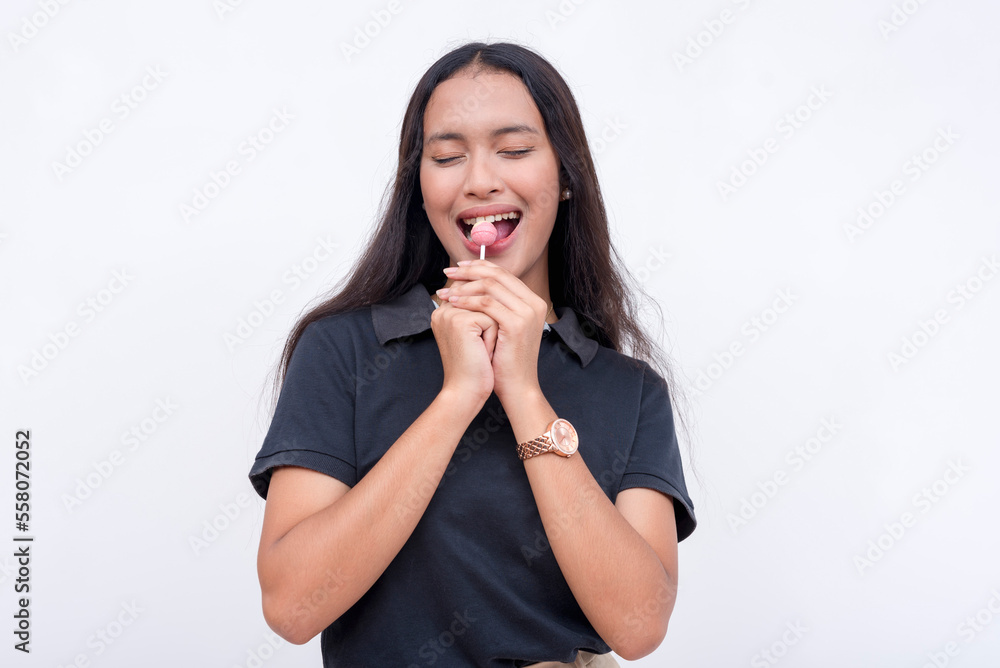 A blissful asian woman holding and tasting a lollipop. Isolated on a white background. A blissful asian woman holding and tasting a lollipop. Isolated on a white background.