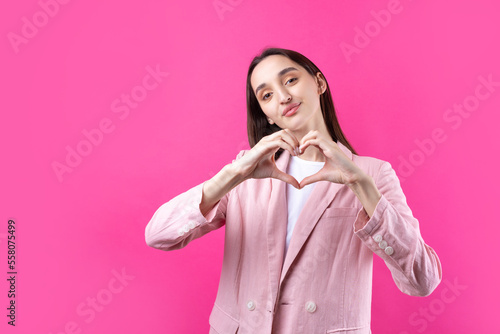 Portrait of a smiling young woman showing heart gesture with her fingers isolated over pikn background photo