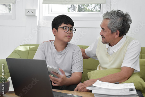Asian senior grandpa and his son are spending times together at home to connect headphone with his laptop to watch and to play online games, soft and selective focus, raising teens concept.