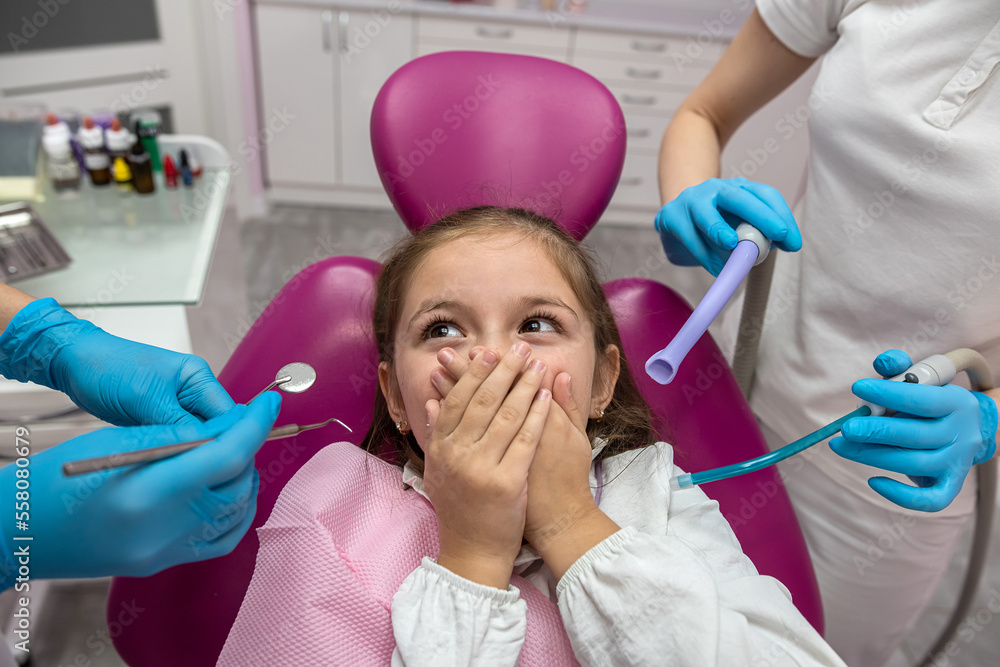 little scared girl covering her mouth with her hands while visiting the dentist. little scared girl covering her mouth with her hands while visiting the dentist.