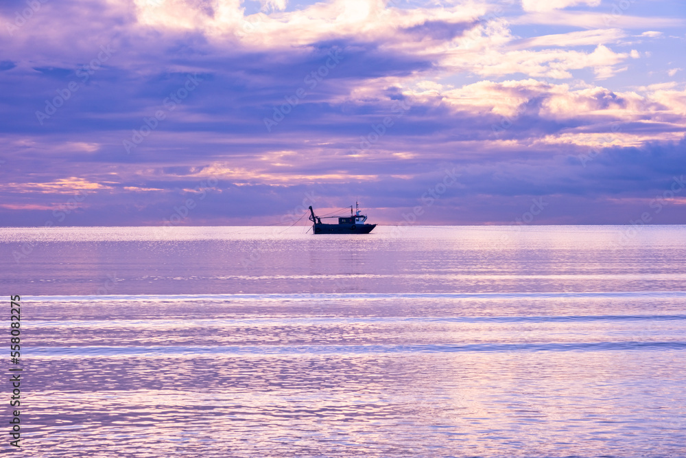 A cold day in Troon Scotland as the sun starts to go down behind the horizon and a loan fishing boat in the Bay