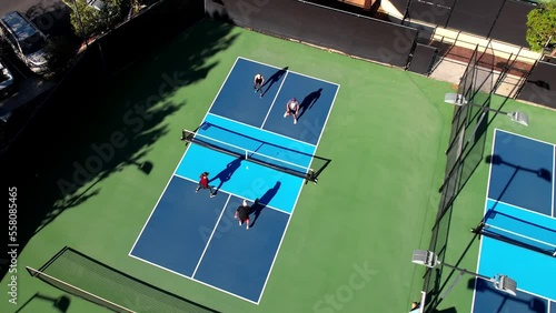 Pickleball match on blue outside court, foursome playing the sport, drone rising over players photo
