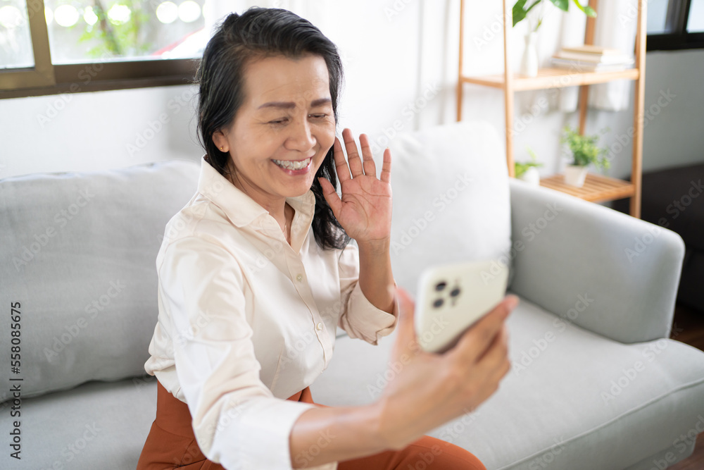 Middle age Asian woman holding cell telephone Work from home. smiling Beautiful mature asian woman VDO Call Conference smart phone with technology concept Middle age Asian woman holding cell telephone Work from home. smiling Beautiful mature asian woman VDO Call Conference smart phone with technology concept