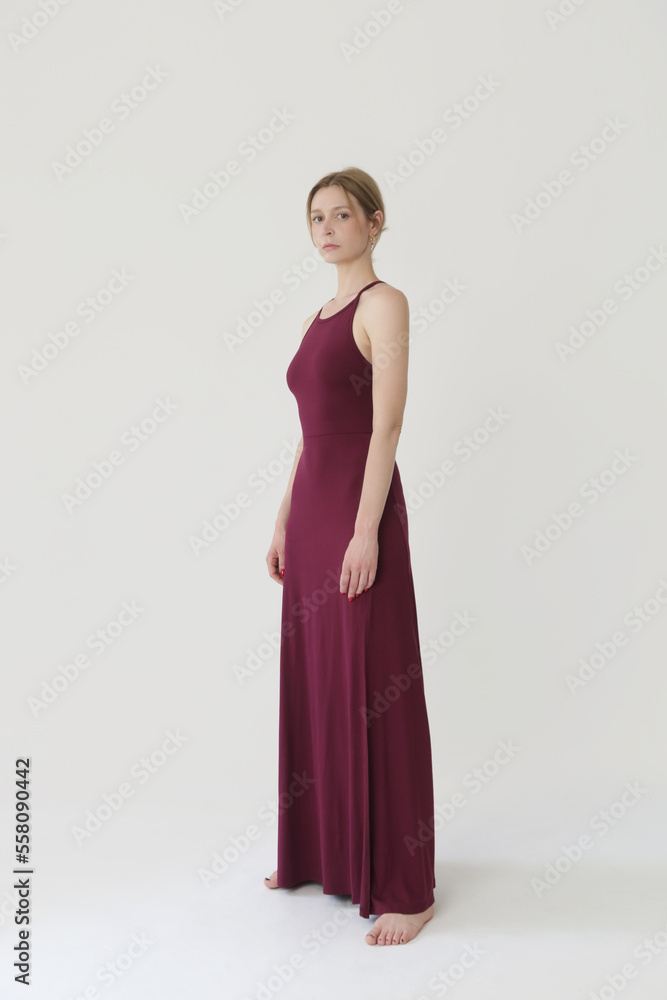 Studio fashion portrait of female model in long tight burgundy jersey dress