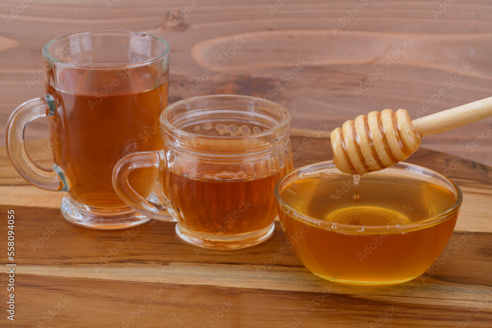 a bowl of honey with honey dipper, glass cup of tea, and honeycomb on wooden table a bowl of honey with honey dipper, glass cup of tea, and honeycomb on wooden table