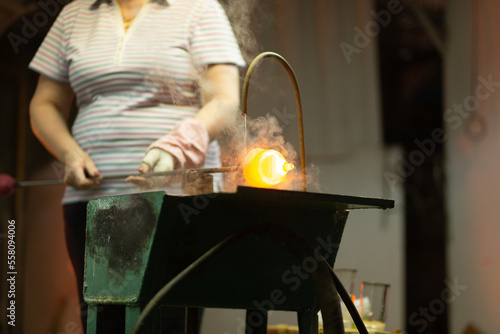 A glass blower is working on the manufacture of glass vases and glasses.