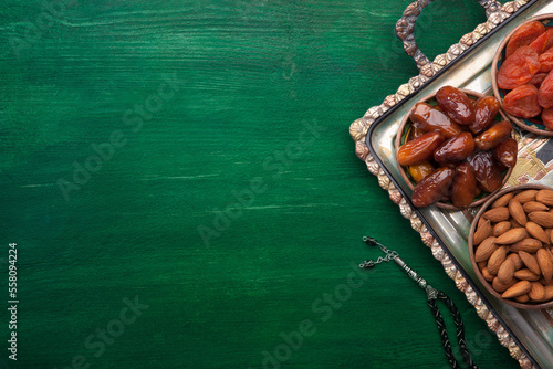 Prayer beads and tray with nuts, dates, dried apricots on dark green  wooden table. Healthy food for breaking Fast in Ramadan. Flat lay photo