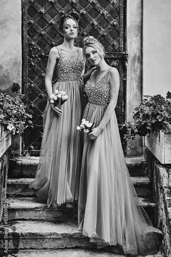 Obraz na płótnie Beautiful bridesmaids in gorgeous elegant stylish floor length v neck chiffon gown dress decorated with sequins sparkles and rhinestones holding flowers bouquets. Wedding day in old beautiful European w salonie