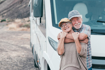 Beautiful senior couple on leisure travel embracing affectionately while standing outside their motorhome. Mature couple enjoying freedom and retirement with an alternative life in motorhome