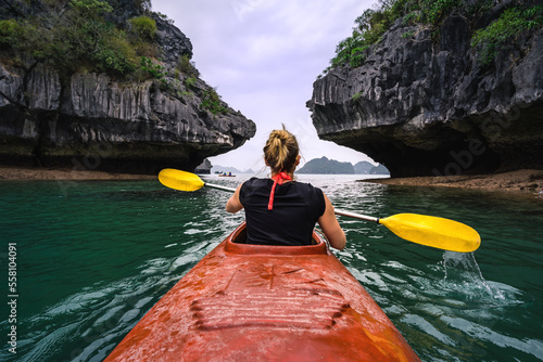 Frau paddelt in rotem Kanu durch eine felsige Bucht.