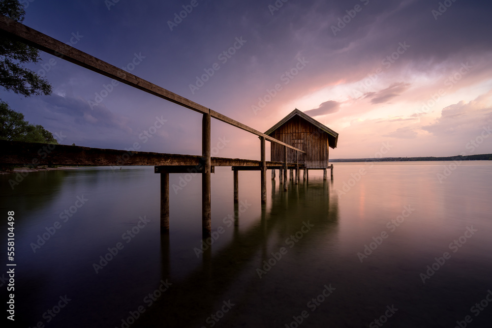 Bootshaus mit Steg am See mit farbigem Himmel.