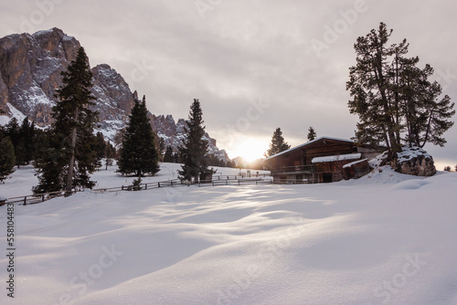 High mountain alpine  hut in winter with snow at the sunset on Dolomites mountain in Trentino Alto Adige, South Tyrol, Italy. Wooden mountain cottage. Mountain house.  © Giulio Benzin