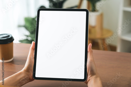 Hands holding digital tablet with mockup of blank screen on sofa in living room.