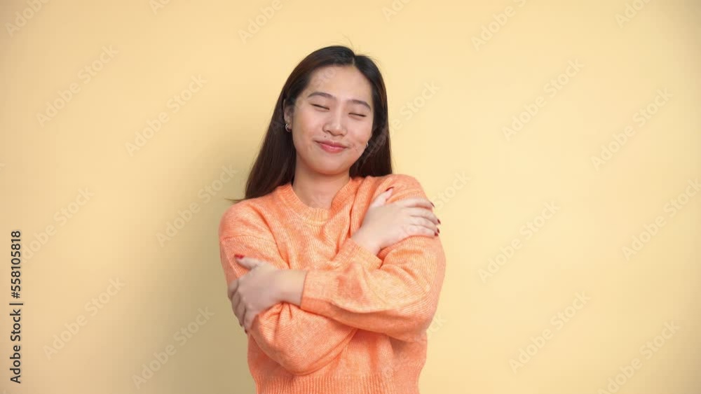 Positive young Asian female in warm sweater smiling and crossing arms while standing against gray background Positive young Asian female in warm sweater smiling and crossing arms while standing against gray background