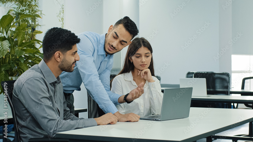 Indian man businessman manager mentor helping coworkers colleagues new employees with laptop teaching partners explaining online job computer software corporate service. Multiethnic teamwork in office