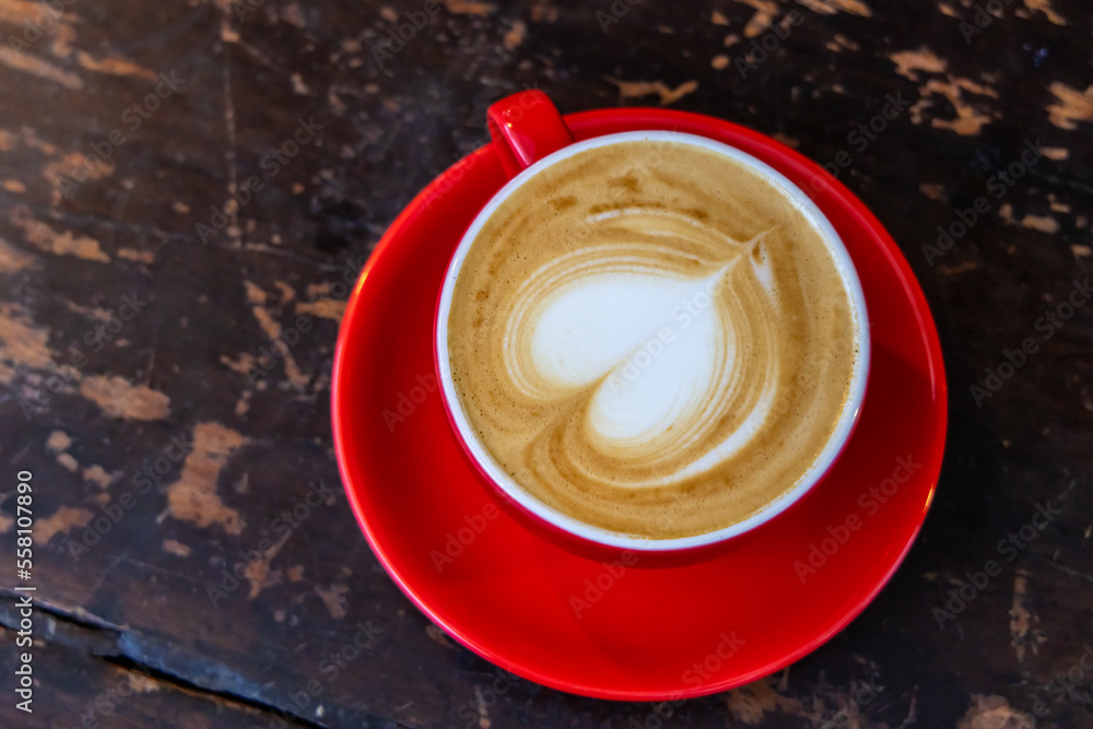 A red cup of coffee cappuccino with latte art on wooden background. Coffee house A red cup of coffee cappuccino with latte art on wooden background. Coffee house