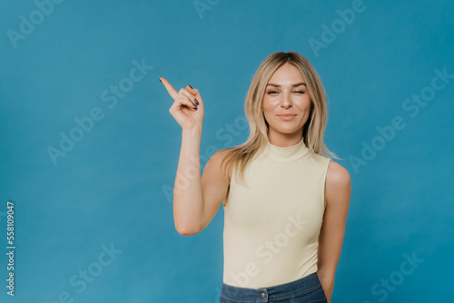 Young cheerful blonde points with her index finger aside to the empty space on the blue background of a light blouse and denim skirt . Make the right choice