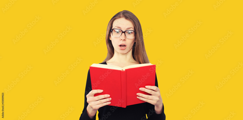 Portrait of shocked student girl in eyeglasses looking in the opened book on yellow background Portrait of shocked student girl in eyeglasses looking in the opened book on yellow background