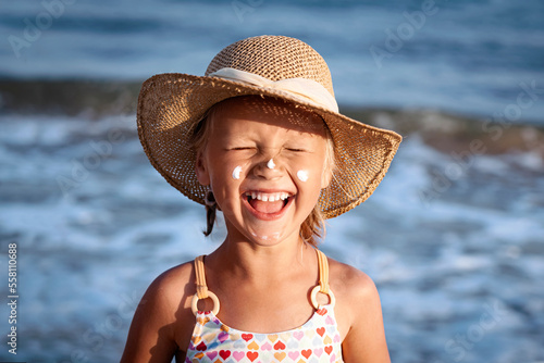 Happy Children Sea Holiday. Smiling Child Girl Sunbathing with Sunscreen on Face in Blue Sea Background. Funny Positive Kid in the Sea photo