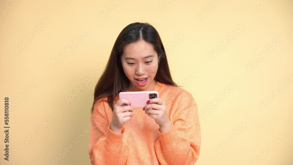 Happy Asian female in casual clothes smiling and browsing smartphone while standing on white background Happy Asian female in casual clothes smiling and browsing smartphone while standing on white background
