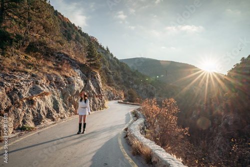 Fototapeta Naklejka Na Ścianę i Meble -  The woman is dear to the mountains. A woman in a white sweater, black boots and a hat walks along a winding alpine path between the mountains at the end of summer at sunset. Travel concept.