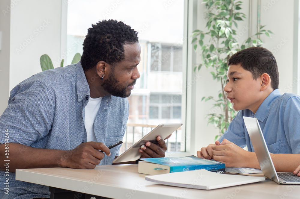 African American teacher and child student studying in classroom. Multiracial male tutor teaching homework lesson to boy pupil in class. Schoolboy back to school and learning with multicultural person African American teacher and child student studying in classroom. Multiracial male tutor teaching homework lesson to boy pupil in class. Schoolboy back to school and learning with multicultural person