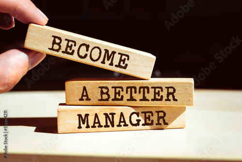 Closeup on businessman holding a wooden blocks with text BECOME A BETTER MANAGER, business concept