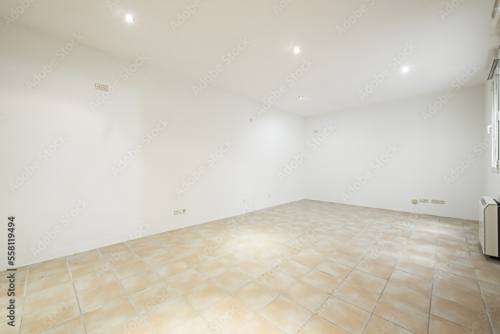 Empty room with light brown stoneware floors, windows and electric heat accumulator Empty room with light brown stoneware floors, windows and electric heat accumulator