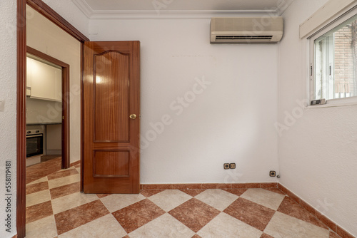 Empty room with air conditioning installation, checkered stoneware floors and varnished sapele wood door