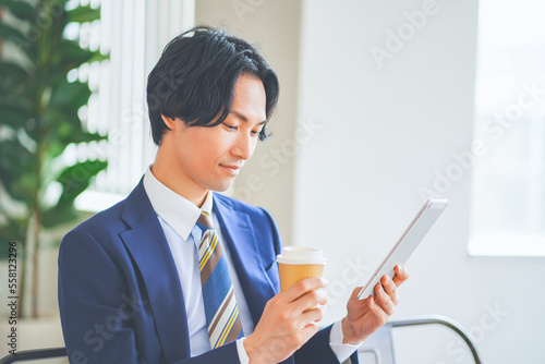 Photos 休憩中にタブレットを見ながらコーヒーを飲むビジネスマン